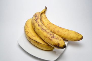 Ugly ripe bananas on the square white plate on white background