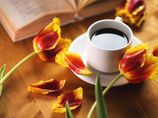 Fototapeta na wymiar A Cup of coffee, beautiful spring tulips and a book on a natural wooden table