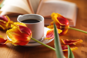 A Cup of coffee, beautiful spring tulips and a book on a natural wooden table