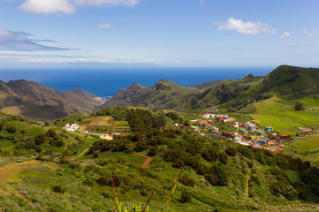 Fototapeta na wymiar Bright green landscape of North Tenerife mountains with blue sea on background. Colorful houses village on valley in Canary Islands, Spain. Sightseeing tour, holidays travel concepts