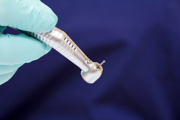 Dentist's hand in green examination glove with dental handpiece.