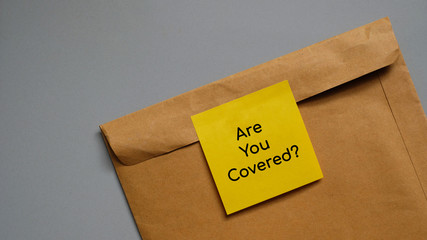 Writing message on Sticky note 'Are you covered' on envelope