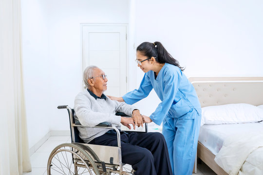Man sitting on wheelchair with nurse in bedroom