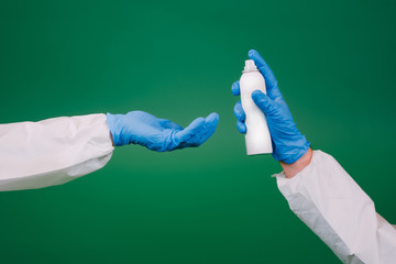 Close up hands in blue gloves of two doctors  clean hands of each other with sanitizer. Coronavirus prevention.  Green background