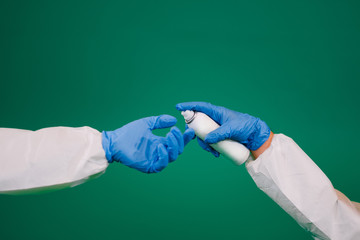Close up hands in blue gloves of two doctors  clean hands of each other with sanitizer. Coronavirus prevention. Green background