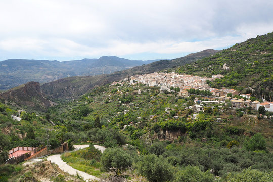 The mountain landscape with the far village with white houses on the green slope and cloudy sky