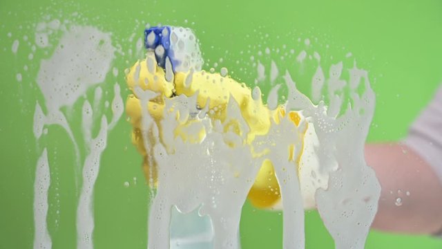hand in rubber glove spraying soap on window glass then wipes it clean with a cloth