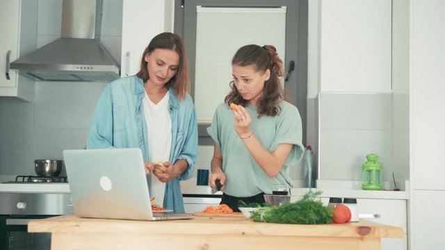 Two young caucasian women talking with friends via the internet while cooking. Friends are doing online cooking classes.