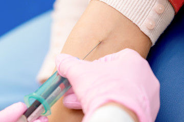 Obraz na płótnie Canvas Nurse takes blood sampling introducing a needle into a vein of woman's arm.