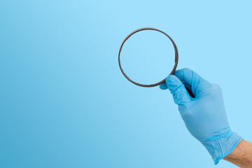hand gesture in a blue medical glove with a magnifying glass isolated, close up, selective focus,...