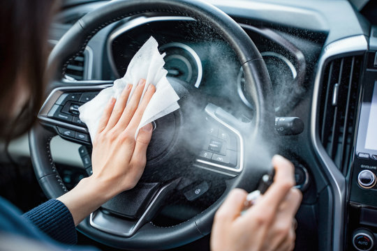 Hands of woman uses disinfectant spray on steering wheel in her car