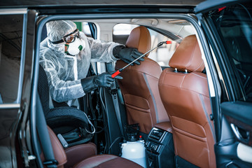 Disinfectant worker in protective mask and suit making disinfection of car seats