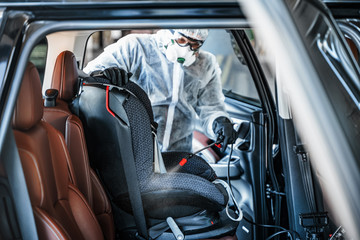 Disinfectant worker in protective mask and suit making disinfection of baby car seat