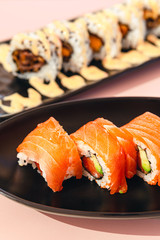 Delicious pieces of salmon and avocado sushi with sauce on a plate with pink background