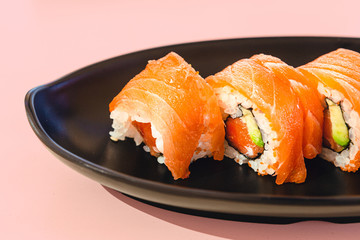 Delicious pieces of salmon and avocado sushi on a plate with pink background