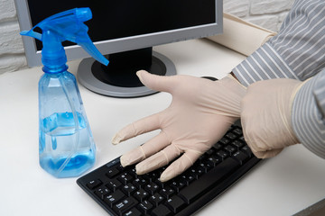concept of cleaning or disinfecting the office - a businessman cleans the workplace, computer, desk, uses a spray gun and paper napkins. Cleaning surfaces from microbes, viruses and dirt.