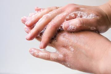 Fototapeta premium Hygiene and protection of hands from viruses (coronavirus) and bacteria using soap. Women's hands with foamed soap close-up on a white background. The process of properly washing hands with soap.