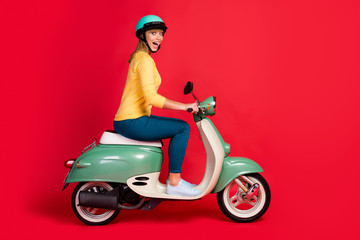 Profile side view portrait of her she nice attractive lovely glad girlish cheerful cheery girl riding moped having fun weekend isolated on bright vivid shine vibrant red color background