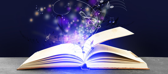 Symphony shining with musical notes from open book on table against dark purple background. Banner...