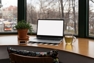 Fototapeta premium Office desk with laptop with mock up and tea, phone near big window. Home office and stay at home. Workspace. 