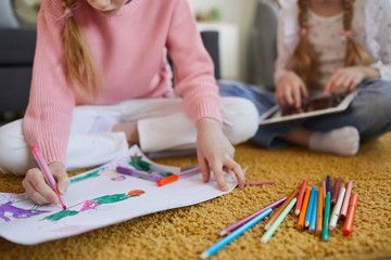 Naklejka premium Close-up of girl sitting on the floor and drawing with colored pencils together with her sister at home