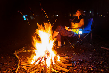 Young woman relaxing near the campfire at night