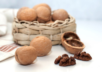 walnuts are in a wicker basket. They lie on a white background next to a white and brown napkin