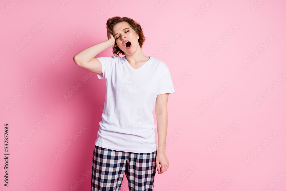 Wall mural Photo of pretty funny tired lady hold hand on head sleepy morning eyes closed don't want go work wear white t-shirt plaid pajama pants isolated pink color background