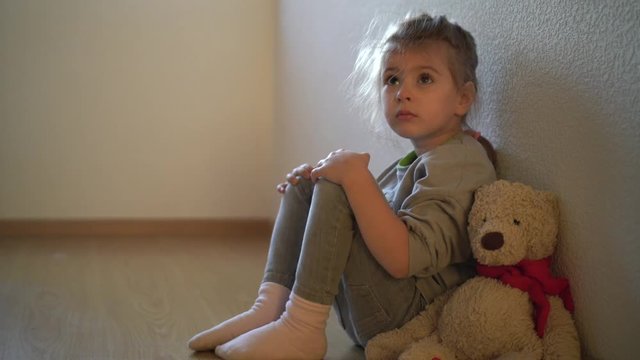  Sad child leaning to the wall by the window. Orphan girl is lonely. Child abuse concept.  Abandoned child.
