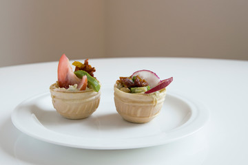 In a plate on a white table are two vegetable tartlets.