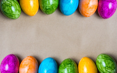 Two borders of easter eggs in different colors on the bottom on brown paper background