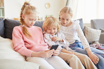 Group of friends sitting on sofa and watching for the game of their friend who using her mobile phone