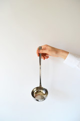 woman holds metal soup ladle in hand on a white background