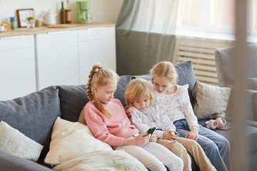 Group of children resting on sofa and using mobile phone together while sitting at home