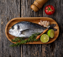 Dorado fish on the wooden  with lime, rosemary, tomato and garlic.  Dorado in the wooden plate. Top view.