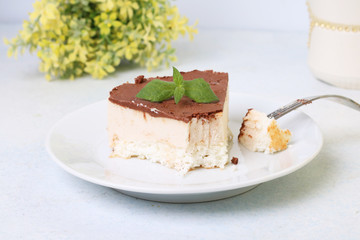 Piece of cake with souffle Birds milk, biscuit, mousse and dark chocolate on a white plate, light background
