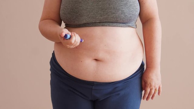 Overweight woman applying diabetes medicine injection into her stomach