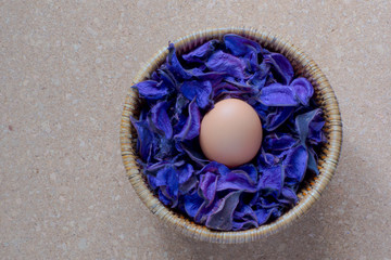 Un huevo rodeado de flores artificiales de lavanda sobre mesa de corcho