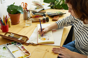 Close-up image of artist drawing in a sketchbook. Female designer working from home. Creative cozy...