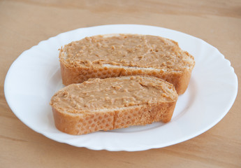 Two peanut butter toasts on a white plate on a wooden table. Close up