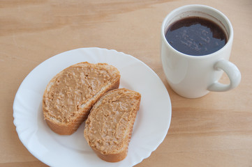 A plate with toasted bread and peanut butter, a cup of coffee on the wooden table close-up
