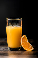 Orange juice is poured into a glass and a slice of orange on a black background