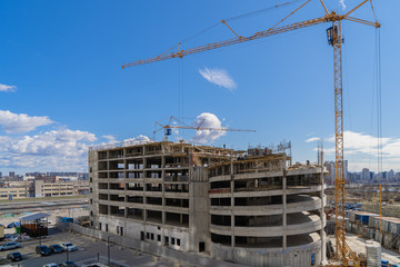 Construction crane at work on a construction site against the blue sky. Construction of a covered Parking lot.