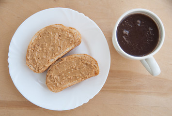 Coffee and peanut butter toasts on a white plate. Wooden table. Top view