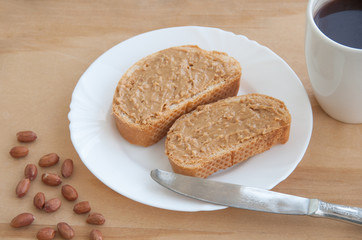Toast with homemade peanut butter on a wooden table. A cup of coffee, knife and peanuts. Top view