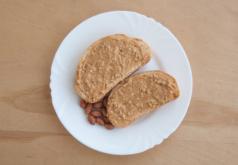 Slices of bread with peanut butter and peanuts for breakfast on a white plate, view from above