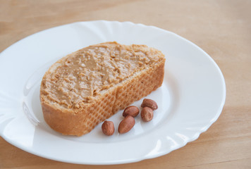 Peanut butter toast with peanuts on a white plate. Wooden background. Close up