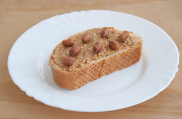 Peanut butter sandwich with peanuts on a white plate. Wooden table. Close up