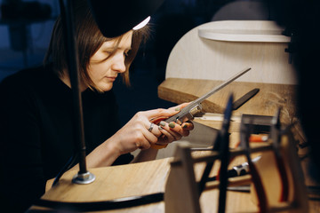 Jeweler working with tools on a piece of jewelry at her workbench. Handicraft people art concept. She makes silver ring. 