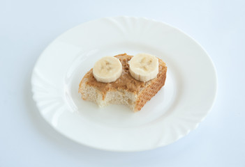 Bitten peanut butter toast with banana on a white plate. Isolated